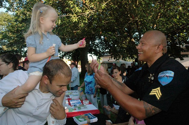 Stan Jones gives his daughter McKenna a boost on his shoulders as she accepts gifts of candy and pencils from Tulalip Tribal Police Sgt. Sherman Pruitt at the Aug. 6 Night Out Against Crime at Comeford Park in Marysville.